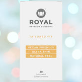A package of Royal Tailored Fit Ultra Thin Vegan Condoms by Royal promotes features such as "TAILORED FIT," "VEGAN FRIENDLY," "ULTRA THIN," and "NATURAL FEEL." It contains 20 lubricated condoms made from natural latex, set against an elegant backdrop with a blurred bokeh effect featuring circular lights.